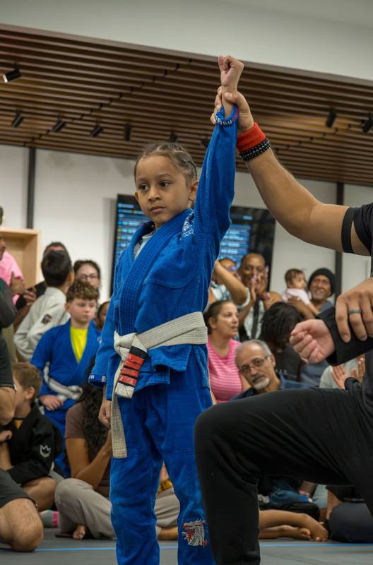 Young girl in a blue gi with her hand raised after winning